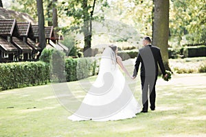 Newly married couple running and jumping in park while holding hands