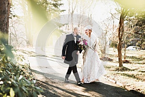 Newly married couple running and jumping in park while holding hands