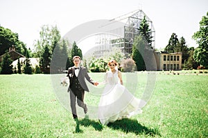 Newly married couple running and jumping in park while holding hands