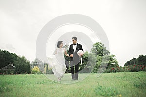 Newly married couple running and jumping in park while holding hands