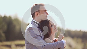 A newly married couple on their wedding day amongst the green nature next to the lake. They are together in the arms of