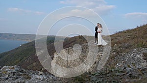 Newly married wedding couple stand near a cliff overlooking the sea.