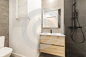 Newly renovated bathroom with black taps, square mirror and light wood cabinet with drawers