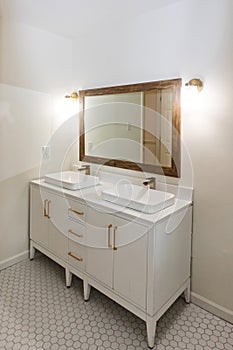 A newly renovated white tiled bathroom with a double sink vanity and gold fixtures