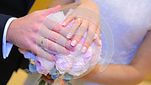 Newly wed couple`s hands with wedding rings. Bride and groom with wedding rings on flowers or wedding bouquet. Newly wed