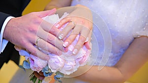 Newly wed couple`s hands with wedding rings. Bride and groom with wedding rings on flowers or wedding bouquet. Newly wed