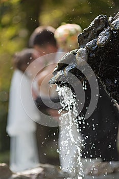 Newly wedded kissing behind fountain