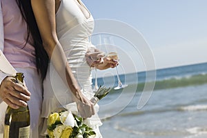 Newlywed Couple With Champagne Bottle And Flutes On Beach