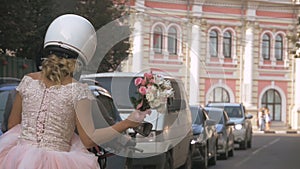 Newlywed couple drive around the city by motorcycle through traffic in summer city. Bride is holding wedding bouquet