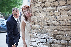 Newlywed couple peek around corner of brick wall, copyspace