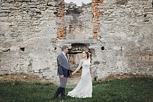 Newlywed couple posing near old castle wall, fairytale wedding at ancient castle outdoors, bride and groom hugging near fortress