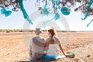 Newlywed couple sitting under shade of tree in summer