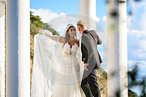 Newlyweds in a beautiful gazebo with columns against the backdrop of mountains and sky