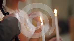 Newlyweds, bride and groom stand and pray in church, holding candles in hands, wedding ceremony