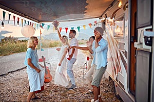 Newlyweds and friends dancing in front of decorated camper rv. Celebration of newlywed love couple. Wedding ceremony, love, nature