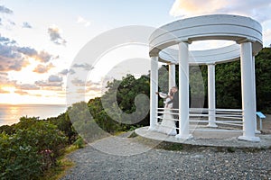 Newlyweds in a gazebo with columns on the seashore in the rays of the setting sun