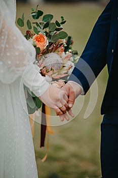 Newlyweds hold hands on the background of a bridal bouquet