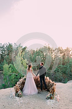 Newlyweds holding hands at the edge of the canyon and couple looking each other with tenderness and love. Outdoors