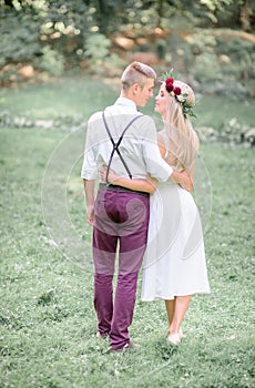 Newlyweds hug each other waists while walking in the grass