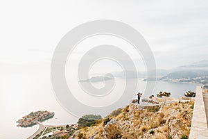 Newlyweds hug on the observation deck, from where you can see the Sveti Stefan island, Budva, Montenegro