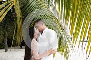 Newlyweds kiss in palm leaves on a white beach