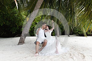 Newlyweds kiss on a swing under a big palm tree