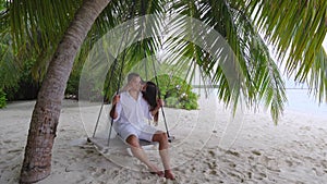 Newlyweds kiss on a swing under a big palm tree.