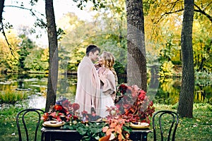 Newlyweds kissing under the plaid next to the festive table. Bride and groom in the park. Autumn wedding. Artwork