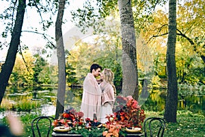 Newlyweds kissing under the plaid next to the festive table. Bride and groom in the park. Autumn wedding. Artwork