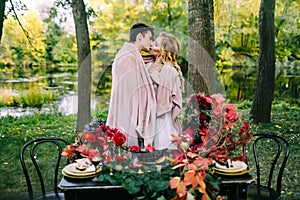 Newlyweds kissing under the plaid next to the festive table. Bride and groom in the park. Autumn wedding. Artwork