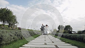 Newlyweds, lovely caucasian bride and groom running along path during wedding ceremony in park