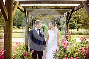 Newlyweds in park rosarium next to beautiful pink roses