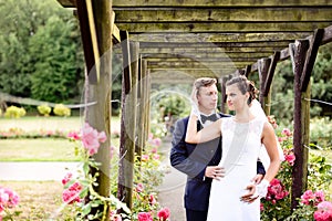 Newlyweds in park rosarium next to beautiful pink roses