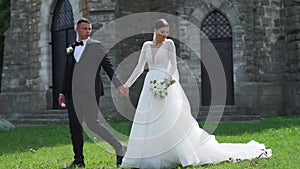 Newlyweds portrait. Lovely Caucasian bride, groom walking near old castle.