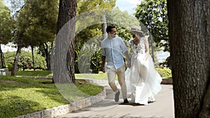 Newlyweds run in park in summer. Action. Beautiful loving couple romantically run away holding hands in park. Wife in