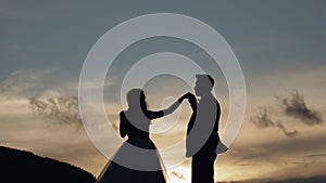 Newlyweds silhouettes bride, groom dancing on mountain slope, holding hands, wedding couple family