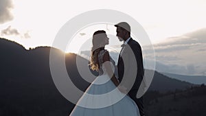 Newlyweds silhouettes bride, groom hugging on mountain slope, holding hands, wedding couple family
