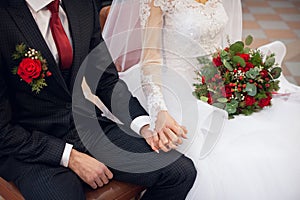 newlyweds sit on a chair with bouquet, hold each other's hands at the wedding ceremony