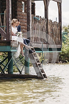 Newlyweds sit on the pier of house above the water