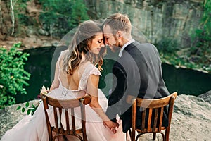 Newlyweds sitting at the edge of the canyon and couple looking each other with tenderness and love. Bride and groom