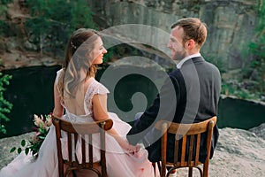 Newlyweds sitting at the edge of the canyon and couple looking each other with tenderness and love. Outdoors wedding