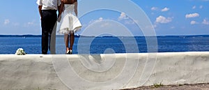 Newlyweds stand holding hands and look into the distance at sea