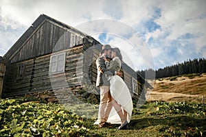 Newlyweds stand and hug on background of old wooden hut in mount