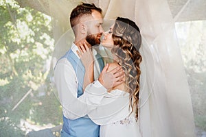 newlyweds stand near a white curtain in a gazebo in the park.