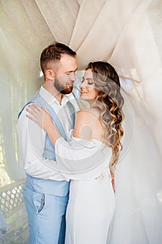 newlyweds stand near a white curtain in a gazebo in the park.