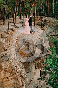 Newlyweds standing at the edge of the rock and couple looking each other with tenderness and love. Bride and groom