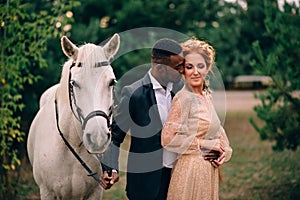 Newlyweds are standing near a white horse