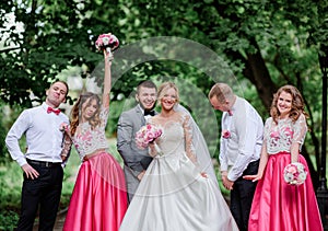 Newlyweds and their friends look happy posing in a bright summer park