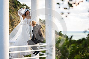 The newlyweds are walking in a beautiful picturesque gazebo, the girl is holding a veil with her hand, the guy is