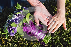 Newlyweds with wedding rings closeup. Couple place their hands on bouquet